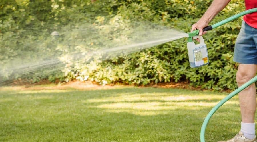Hombre fertilizando el césped del patio trasero residencial con un esparcidor químico líquido.  Paisajista rociando césped con fertilizante, herbicida e insecticida.